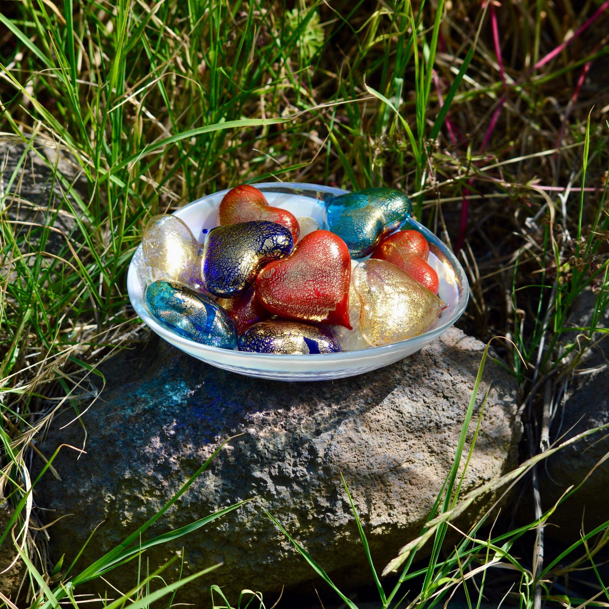 Set of three small Murano glass heart figurines in red, white, and blue colors, made in Italy, displayed in a bowl.