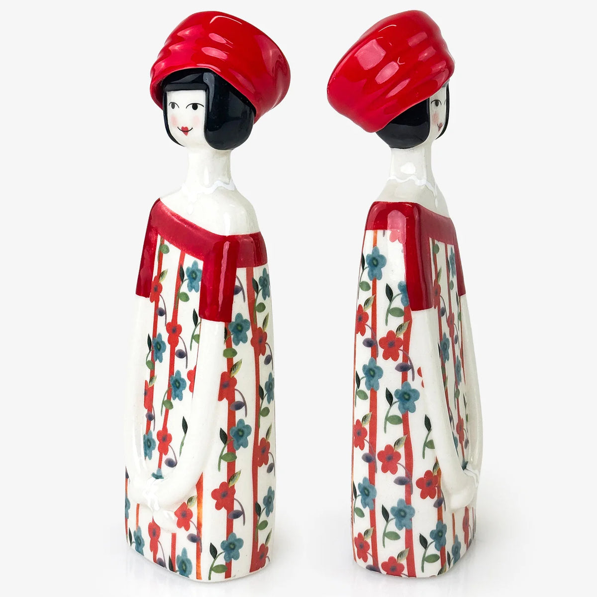 Two ceramic figurines of stylized women wearing red hats and red-and-white patterned dresses with blue floral accents, shown on a light gray background.
