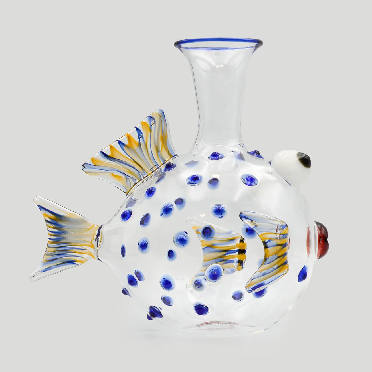 A clear glass fish-shaped water decanter with blue and yellow striped fins, blue glass dots, shown on a plain light gray background.