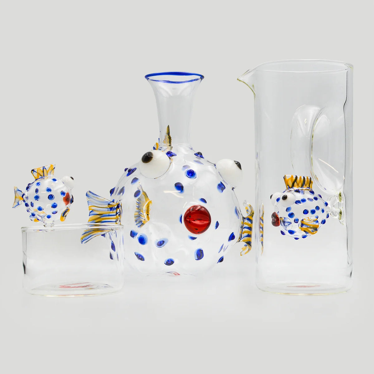 A set of hand-blown glass featuring a central fish-shaped decanter with blue and white polka dots accompanied by a matching carafe, and a small bowl.