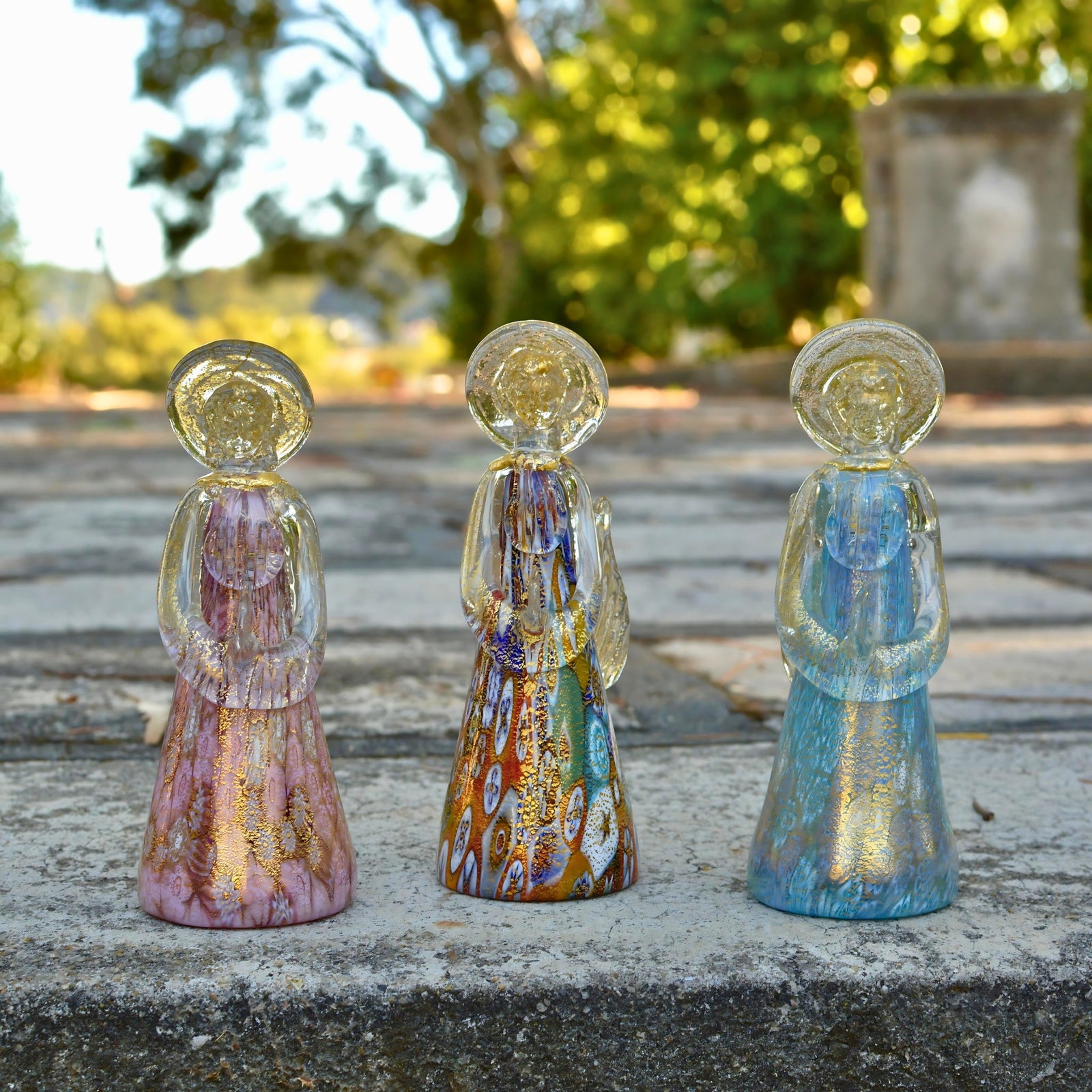 Three colorful Murano glass Millefiori angels with 24-karat gold foil accents, displayed on stairs, handmade Italian figurines.