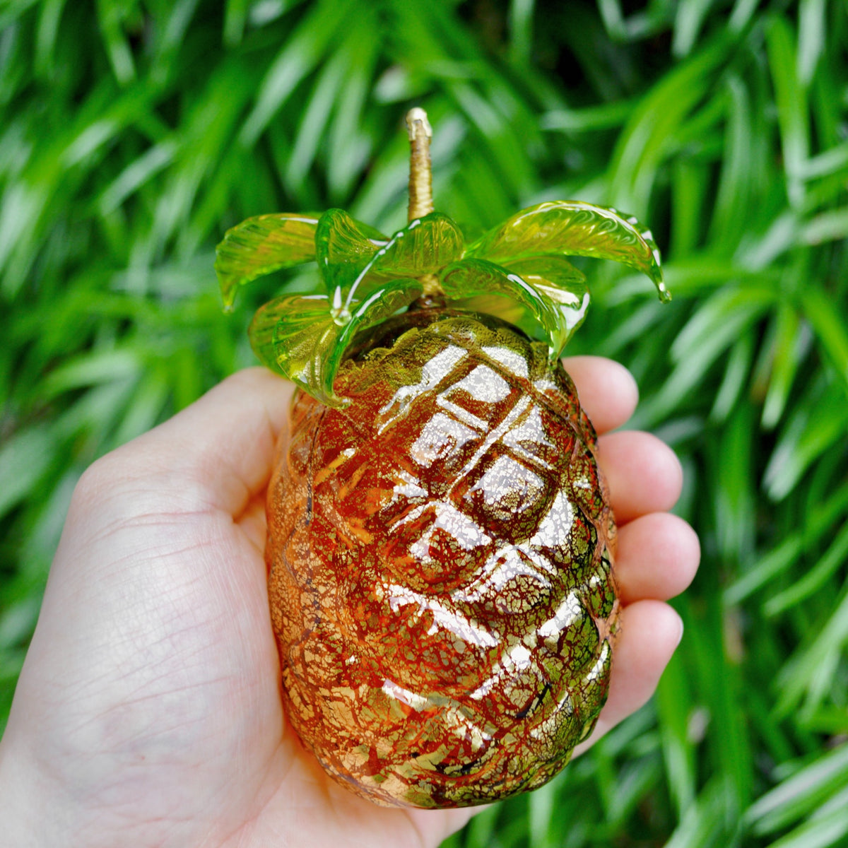 An amber colored glass pineapple with green leaves held in a hand.