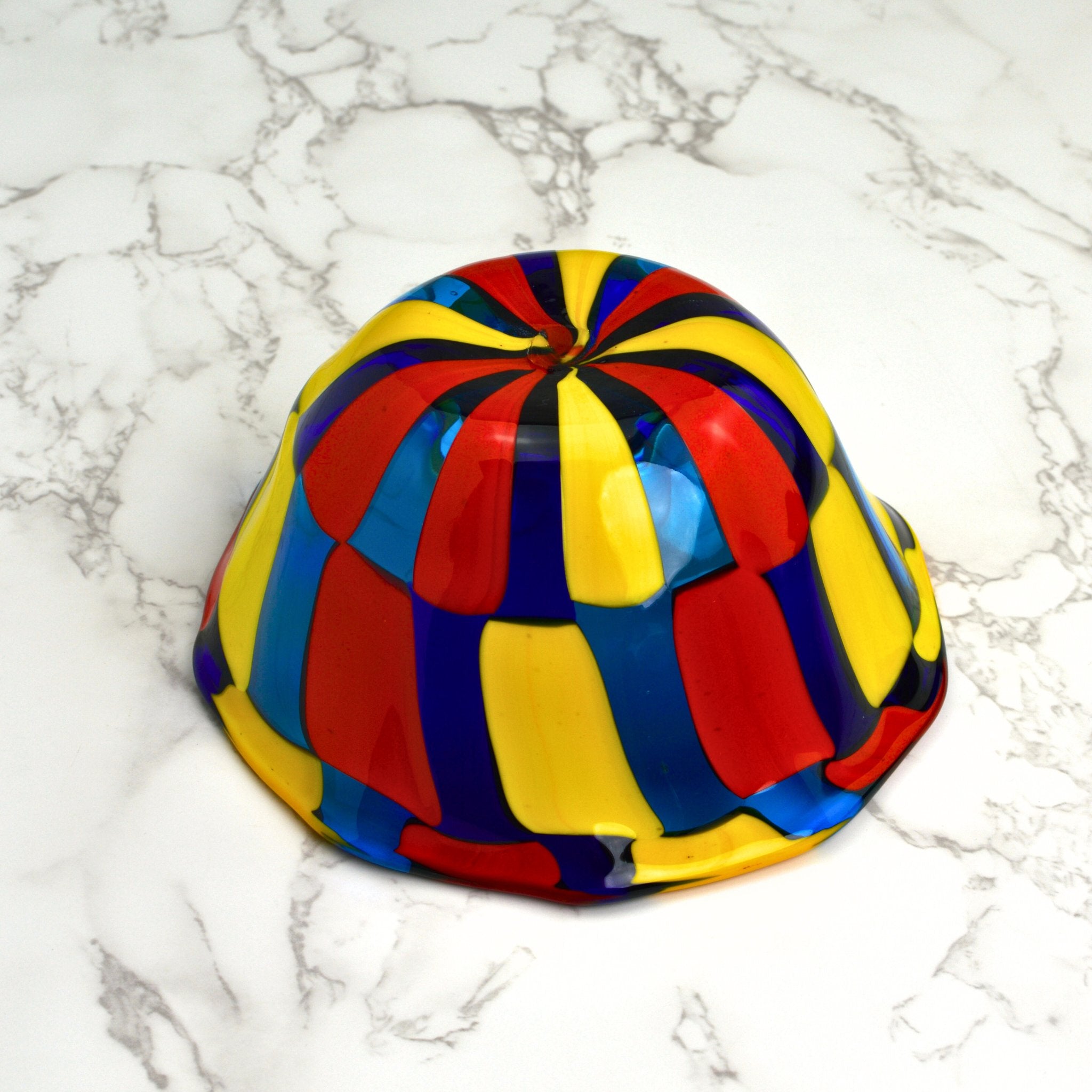 A Murano glass bowl in bright colors sits upside down on a tabletop.