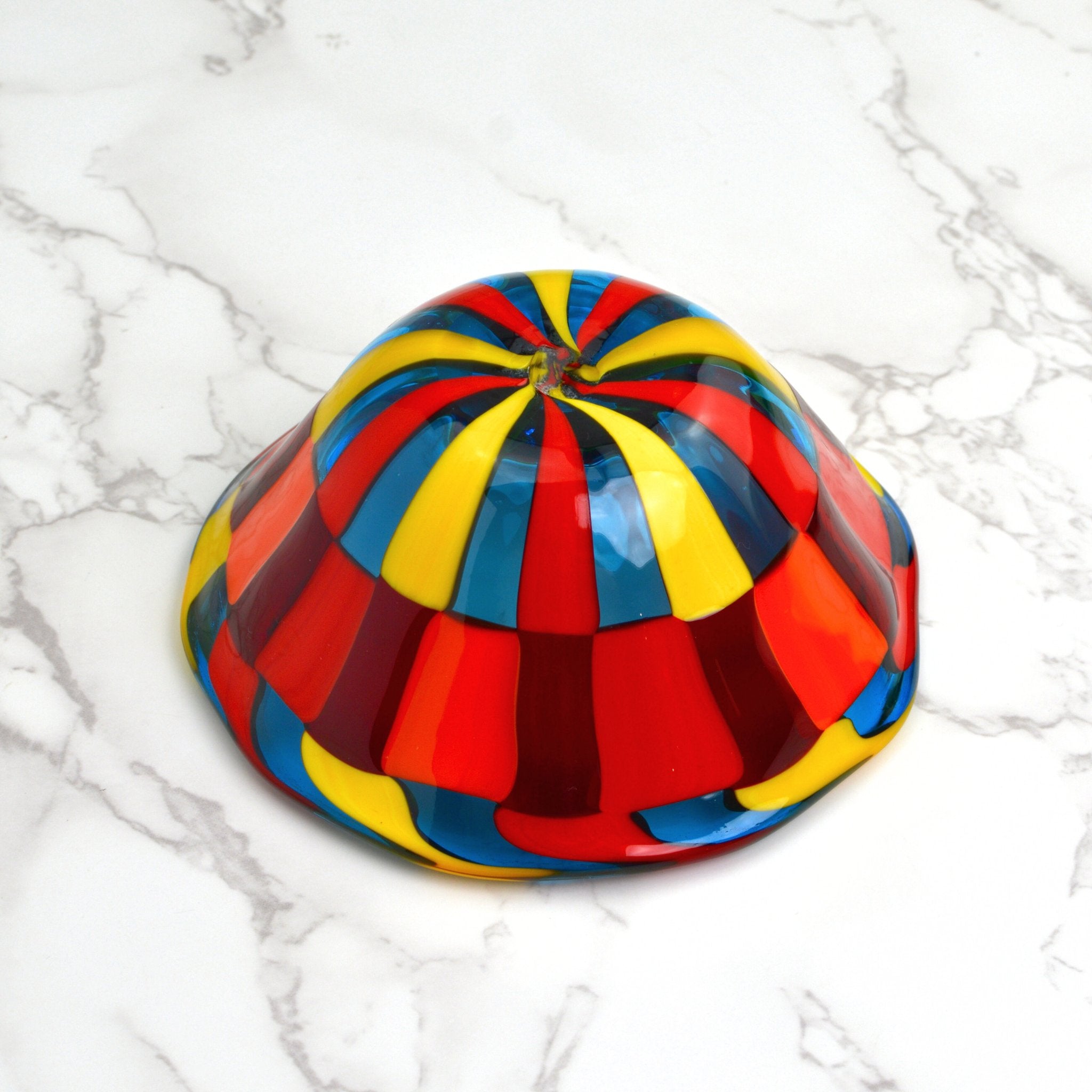 A Murano glass bowl in bright red, blues, and yellows sits upside down on a tabletop.