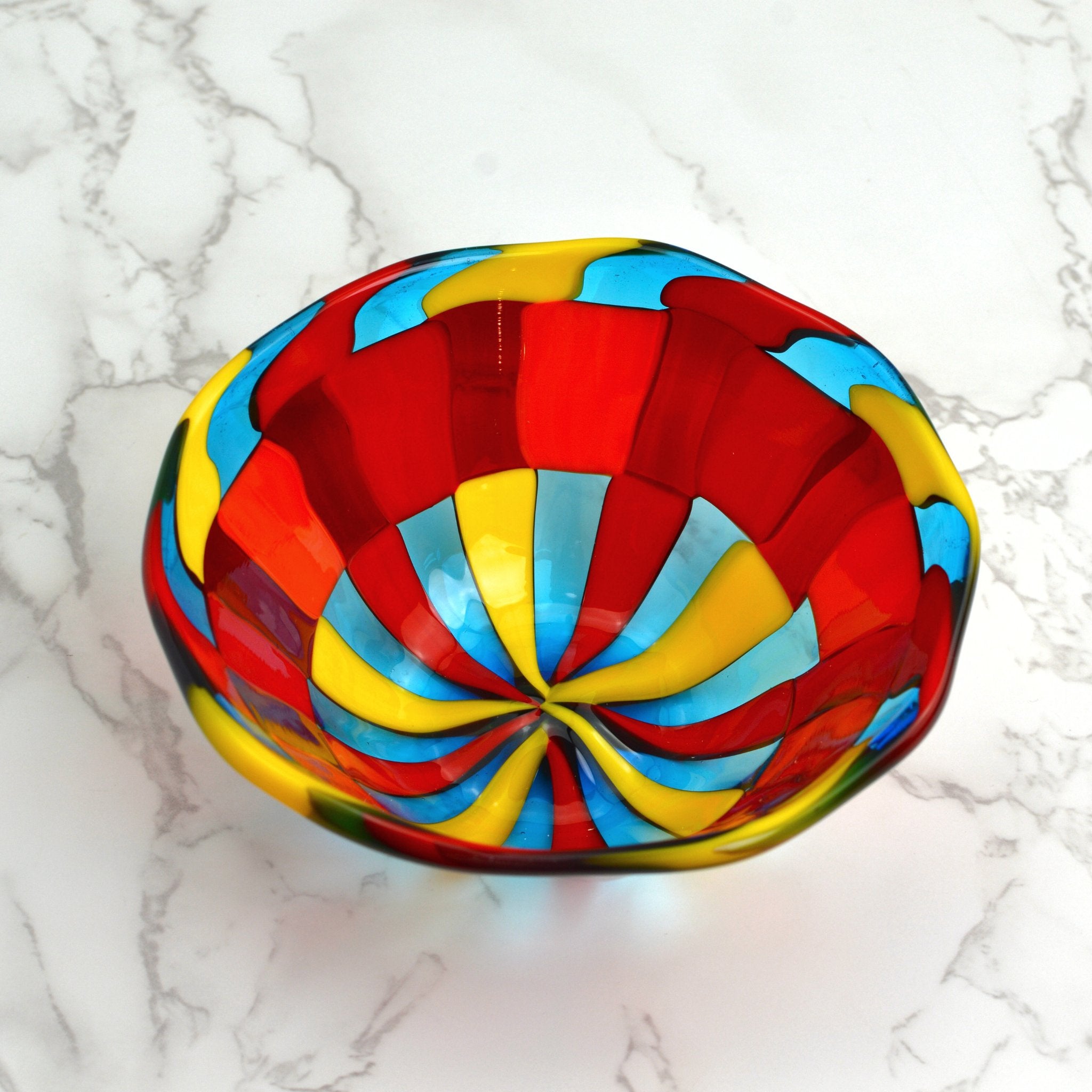 A Murano glass bowl in bright colors sits on a tabletop.