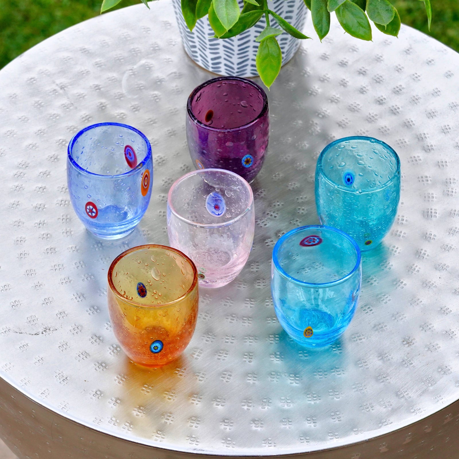 Set of six Serena Murano glass shot glasses with colorful millefiori patterns, made in Italy, displayed on a metal table.