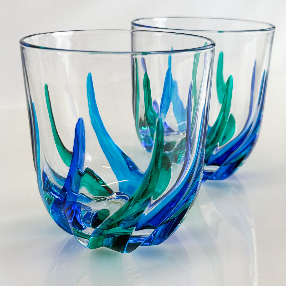 Two glass tumblers with blue and green artistic designs on a white background