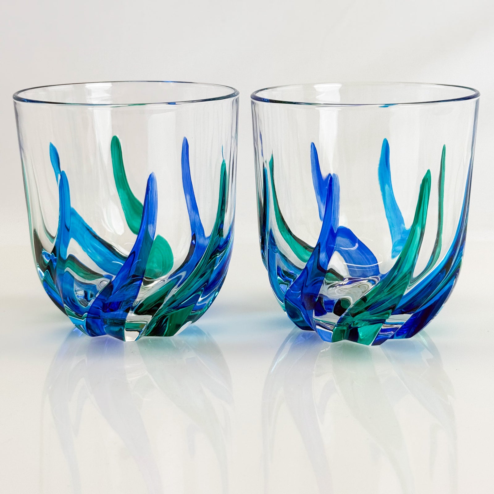 Two glass tumblers with blue and green artistic designs on a white background