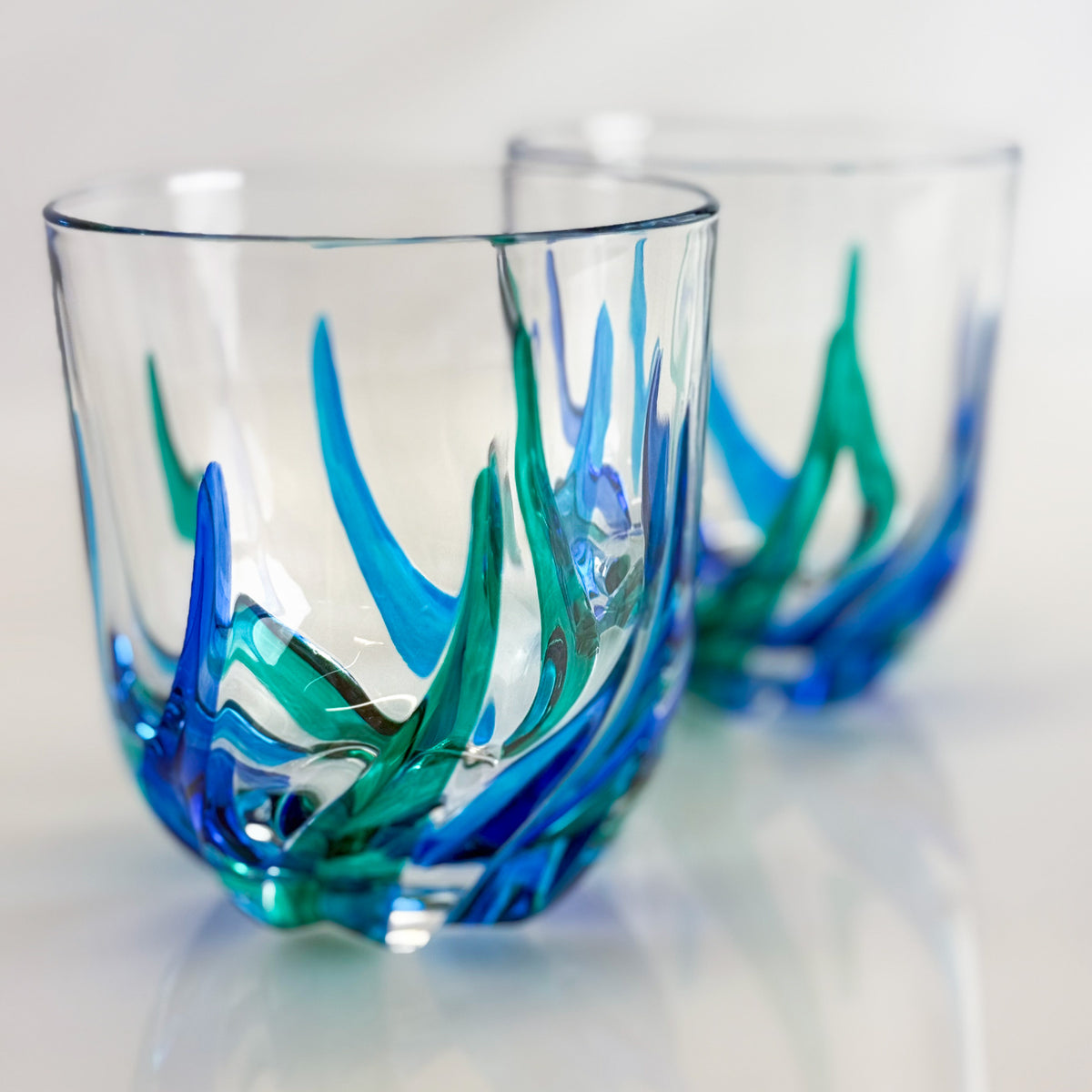 Two glass tumblers with blue and green artistic designs on a light background