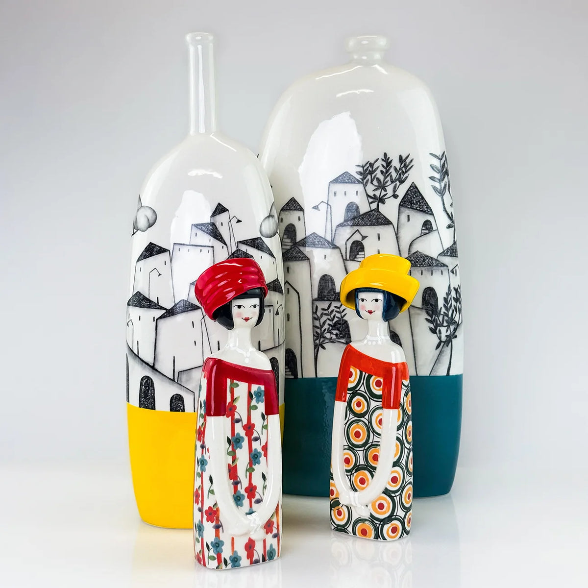 Two decorative ceramic vases with hand-painted village scenes and stylized female figures, displayed on a clean white background.