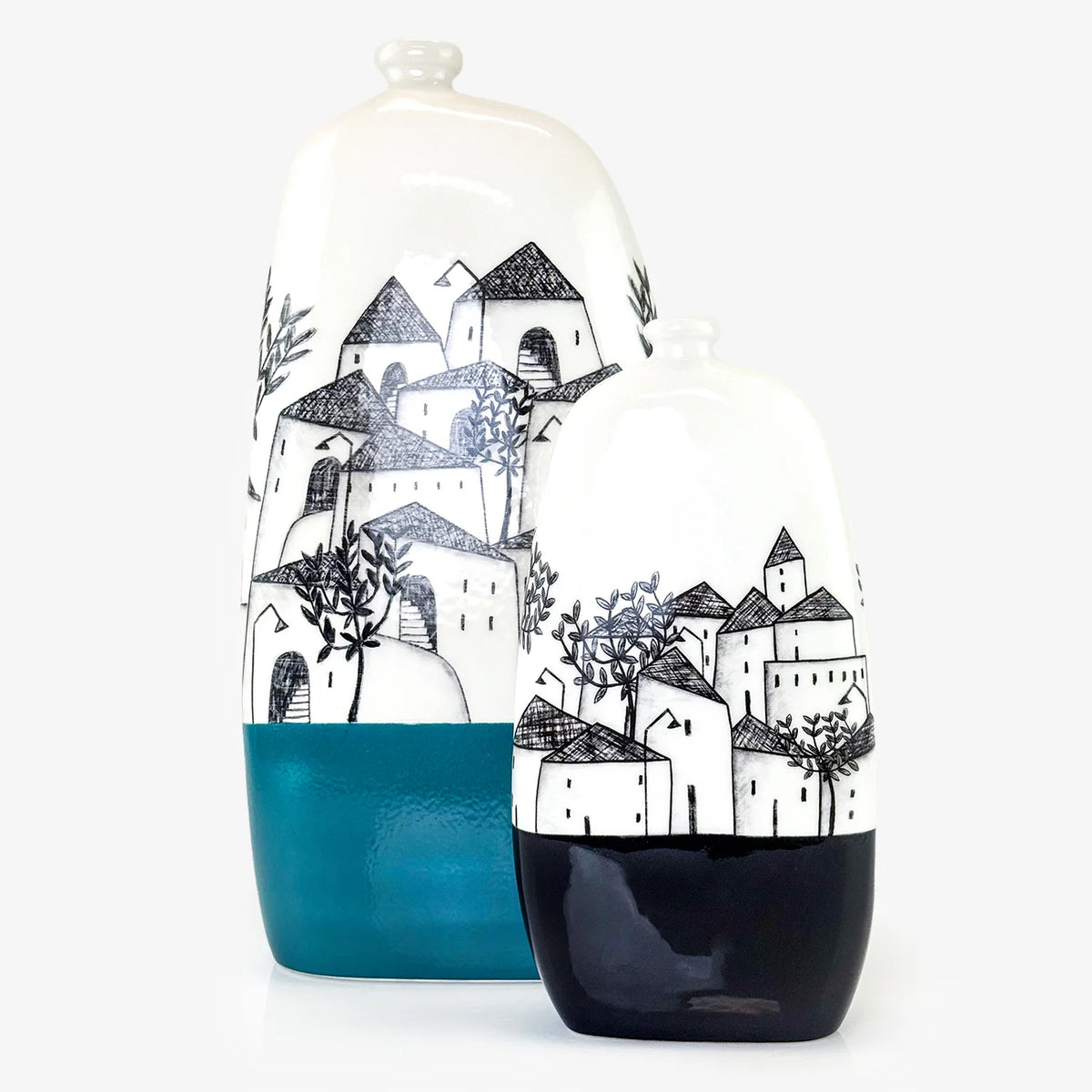 Two ceramic decorative vases with a hand-painted black and white village design, featuring a teal blue lower section and a glossy black lower section on the smaller vase, set against a plain white background.