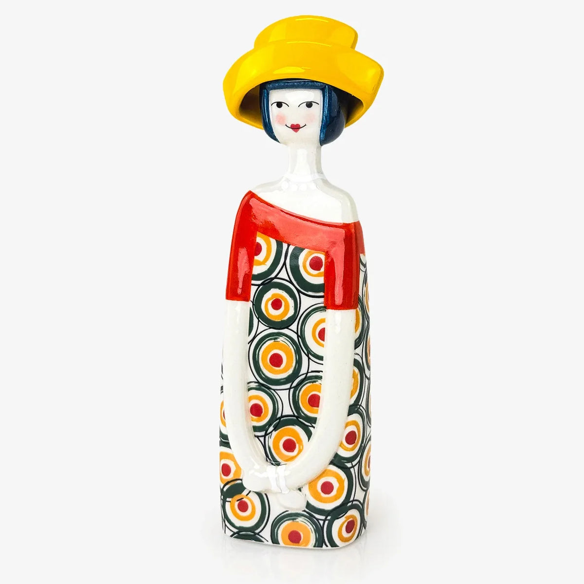 A decorative ceramic figurine of a stylized woman wearing a bright yellow hat, a red top, and a black dress with a colorful concentric circle pattern, set against a plain light gray background.