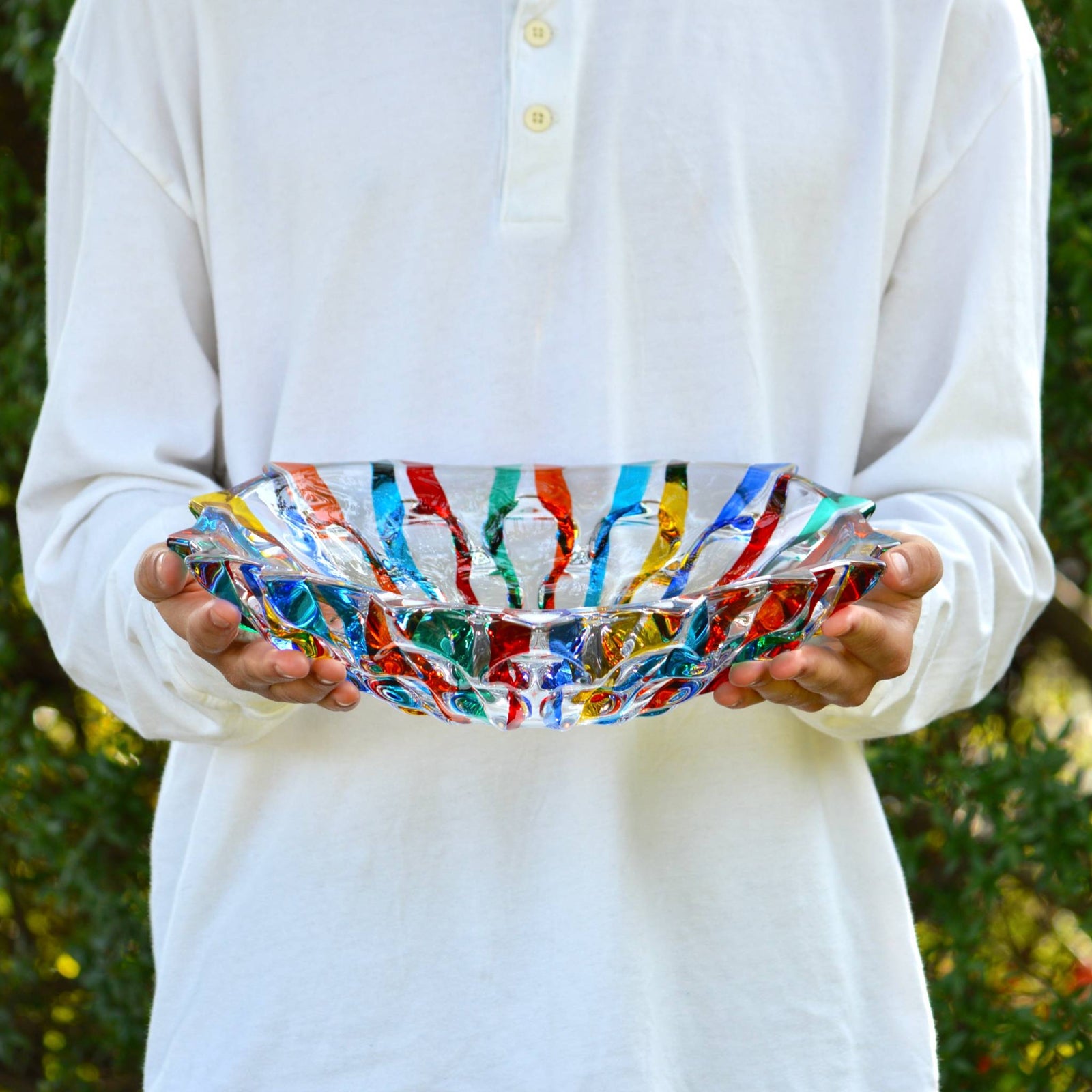 Hand holding a large, round, hand-painted glass decorative bowl by DZ, made in Italy, showcasing vibrant artistic design.