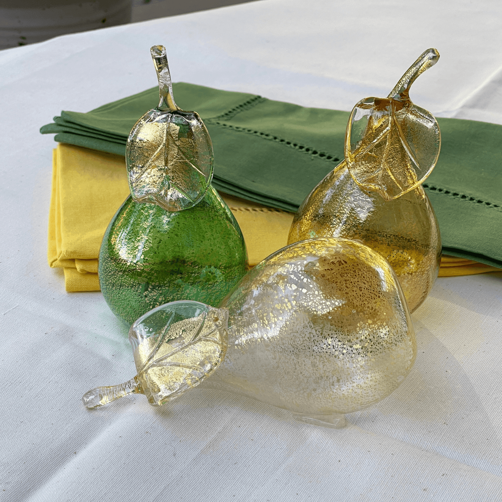 Three life-size Murano glass pears, colorful blown glass artificial fruit from Italy, displayed on a neutral surface.